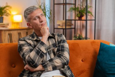 Düşünceli, zeki, beyaz saçlı, çenesini ovuşturan, düşünceli bir beyaz adam. Düşünceli bir ifadeyle yan yana bakıyor. Evdeki dairede şüpheli bir sorunun çözümünü düşünüyor. Genç adam kanepede oturuyor.