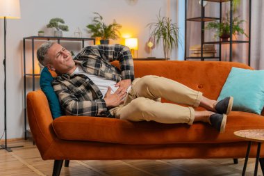 Genç, beyaz bir adam kanepeye uzanmış karın ağrısı ve mide iltihabı şikayeti yaşıyor. Semptom zehirlenmesi geçiren bir adam ishal hazımsızlık peptik ülser pankreatiti geçiriyor..