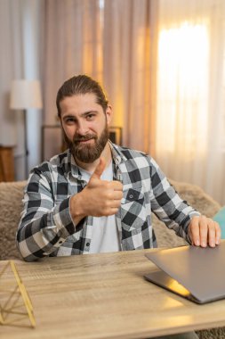 Mutlu gülümseyen genç adam ev masasındaki görevlerini tamamlıyor, bilgisayarını minnettar bir ifadeyle kapatıyor. Kanepede oturan beyaz bir adam kameraya doğru dönüyor, iyi bir iş çıkardığını söylüyor..