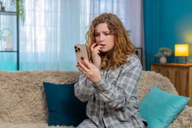 Evde endişeli bir şekilde önemli bir mesaj bekliyor. Akıllı telefonu kaydırırken tırnağını yiyor. Kanepede oturan beyaz saçlı kız gergin, stresli, duygusal beklenti, gerilim anı
