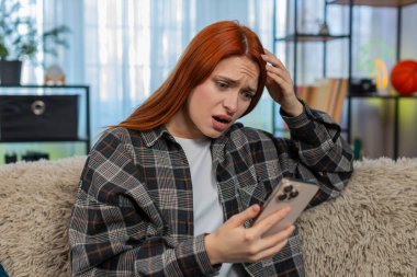 Evde elinde akıllı telefon olan genç bir kadın kötü haberden sonra üzgün bir suratla ekrana bakıyor. Kanepedeki beyaz saçlı kız üzgün hissediyor, mesajlara duygusal tepki veriyor ya da beklenmedik sonuçlar veriyor.