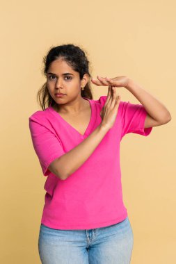 Hintli bir kadın elleriyle kameraya dikkatlice bakarak kısa bir ara vererek mola veriyor. Bej arka plandaki kız dikkat gerektiren mola, dinlenme ya da geçici duraklama ihtiyacını açıkça gösteriyor