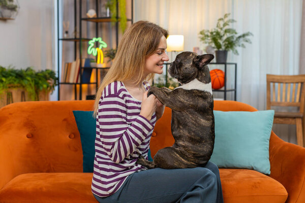 Middle-aged woman brings face close to French bulldog at home smiles happy portrait close view tender bond. Girl with dog on sofa enjoys cuddle touch care and affection cozy comfort, relaxing, rest