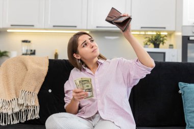 Evdeki genç kadın cüzdanın içine baktığında az miktarda nakit para görüyor ve yoksulluk ve borçtan rahatsız oluyor. Kanepede oturan beyaz kız gol atmayı planlıyor. Maliyetleri ve bütçeyi düşürüyor ve endişeli ruh hali ve stresi gösteriyor.