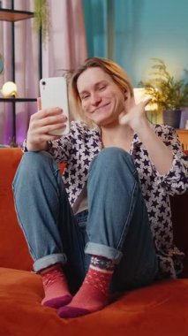 Kafkasyalı mutlu bir kadın akıllı telefondan video görüşmesi yapıyor ve el sallayarak selam veriyor. İletişim, toplantı. Gülümseyen kız blogcu cep telefonuyla konuşuyor evdeki kanepede oturuyor..