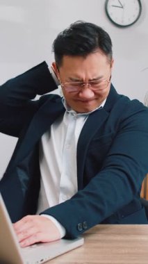 Orta yaşlı, yorgun Asyalı iş adamı ev işyerinde dizüstü bilgisayarla çalışırken omurga kası ağrısından muzdarip. Çok çalışıyorum. Serbest çalışan takım elbiseli Çinli adam masaj yaparak acıyı dindirmeye çalışıyor.