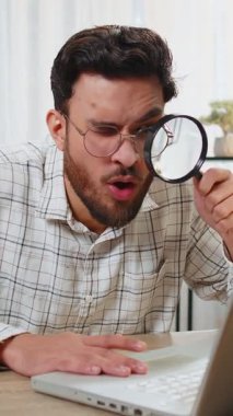 Ofiste çalışan araştırmacı şaşkın iş adamı elinde büyüteçle dizüstü bilgisayarın ekranına bakıyor. İfade ediyor, arıyor, analiz ediyor. Ofisteki profesyonel serbest çalışan.