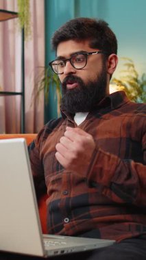 Laptop bilgisayar kullanan Hintli genç adam, iyi haber mesajı alıyor. Aniden kazanılan piyango galibiyetini kutluyor. Evdeki kanepede online alışveriş oyunu oynuyor.