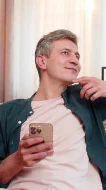 Evdeki genç adam, akıllı telefondaki eski aile fotoğraflarına bakarken koltukta sıcak bir şekilde gülümsüyor. Beyaz adam nostaljik duygulardan ve yumuşak anılardan hoşlanıyor. Akrabaları ve çocukluk günlerini düşünüyor.