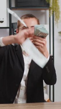 Resmi takım elbiseli neşeli zengin genç işadamı kameraya bakarak para harcıyor, daha fazla bahşiş, büyük kar, başarı kazanan piyango, alışveriş. Ofis masasında çalışan mutlu serbest çalışan bir erkek..