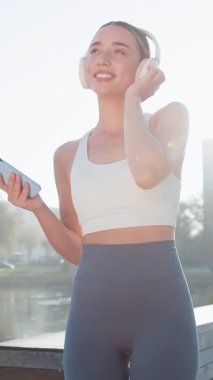 Atletik fitness sporu koşucusu kız antrenmanı, akıllı telefon tutmak kulaklıkla müzik dinlemek, dans etmek, eğlenmek. Parkta egzersiz kardiyolojisi. Danstan hoşlanan genç bir bayan koşucu. Aktif sporcu kadın