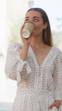 Kafkasyalı mutlu genç kadın sabah kahvesini içiyor sıcak bir şeyler içiyor ve dışarıda gülümsüyor. Dinleniyorum, ara veriyorum. Şehir merkezi caddesinde yürüyen ve kahve içen bir kız. Kasaba yaşam tarzları.