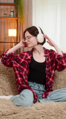 Genç, mutlu kulaklıklı bir kadın evdeki kanepede heyecanla dans ediyor. Keyif ve ritimle en sevdiği şarkıya özgürce geçiyor. Kız enerjiyi, eğlenceyi ve mutluluğu ifade eder, müziğin canlandırıcı gücünden zevk alır.