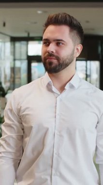 Resmi giyinmiş kendinden emin erkek işadamı kameraya bakıyor ve gülümsüyor. Yakışıklı bir ofis çalışanı modern lobide mutlu ve kollarını kavuşturmuş duruyor. İş adamlarının portreleri..