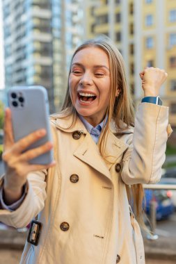 Cep telefonu kullanan Kafkas iş kadınının şehir merkezindeki akıllı telefon bahsini kazanan kadını şaşırtarak zafer başarısını kutlamasına şaşırdım. Şehir sokağında duran kız.
