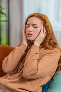 Hasta kızıl saçlı kadın baş ağrısı problemini tedavi etmek için tapınakları ovuyor, tansiyon ve migren stresinden muzdarip evde acı içinde kıvranıyor yüksek tansiyon. İçerideki küçük kız kanepede yatıyor. Dikey