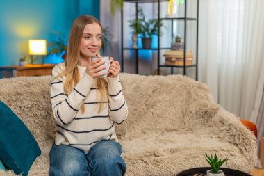 Beyaz bir kadın, elinde sıcak çay fincanıyla evinde oturuyor ve dinleniyor. Sıcak bir içecek, sakin ve rahat bir ortam sağlar. Stres, modern yaşam tarzını rahatlatır. Huzurlu bir ortam.