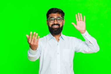 Hintli adam neşeli bir ifadeyle el sallıyor, birini daha yakına gelmeye ya da hoş geldin jesti ile içeri girmeye davet ediyor. Yeşil renkli arka plandaki Arap adam gülümseyerek dikkat çekiyor..