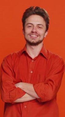 Gülümseyen mutlu beyaz adam göz kırpıyor, kameraya gülümsüyor, göz kırpıyor, flört ediyor, iyimserliğini dile getiriyor, iyi haberler var. Stüdyonun turuncu arka planında izole edilmiş yakışıklı genç bir adam.