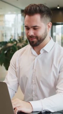 Modern ofis lobisinde kameraya bakıp gülümseyen mutlu sakallı iş adamının portresi. Resmi gömlekli genç bir erkek yönetici. İnternette dizüstü bilgisayarda çalışan yakışıklı bir adam otel odasında oturuyor..