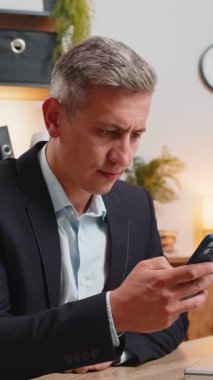 Üzgün genç işadamı, ofis masasında akıllı telefondan kötü haberler okuyor. Resmi takım elbiseli üzgün erkek işveren hoş olmayan tebligattan rahatsız, internetteki bilgiden şok olmuş, mesajla depresyona girmiş..