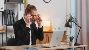 Yorgun ve genç bir iş adamı. Gözlüklerini çıkarıyor. Kuru gözlere masaj yapıyor. Ofiste dizüstü bilgisayar kullandıktan sonra aşırı çalışan adam göz yorgunluğu çekiyor. Baş ağrısı, görsel yorgunluk ve göz ağrısı konsepti.