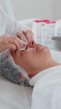Kozmetik doktoru, temizlikçi kadın yüzü, kaplıca salonundaki pamuklu mendilli gözler. Kız teninin kozmetik güzellik prosedüründen önce temizlenmesi. Güzellik uzmanından yüz bakımı. Dikey yakın plan portre