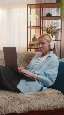 Genç bir kadın evde serbest çalışmaktan, dizüstü bilgisayarla yazmaktan ve kulaklıklarla sessiz müzik dinlemekten hoşlanıyor. Kanepede dinlenen kız, sıcak gün batımı, rahat, profesyonel ve yaratıcı bağlılık.