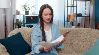 Evde oturan genç kadın, finansal sorunlar yüzünden hayal kırıklığına uğramış faturaları ve faturaları savurarak stresli bir şekilde kanepeye oturdu. Kafkasyalı kız üzgün, duygusal olarak bitkin, maddi sıkıntılar ve stresle boğulmuş.