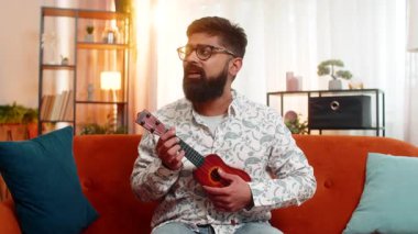 Hintli adam evinde kanepede oturuyor, gülümsüyor ve neşeyle ukulele çalıyor, ilham verici ve yaratıcı olarak özgür hissediyor. Arap adam müziği mutlu bir şekilde doğaçlıyor, içeride eğlenceli ve olumlu duyguları ifade ediyor..