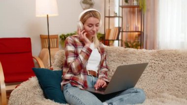 Genç yetişkin bir kadın evdeki kanepede otururken bilgisayarında en sevdiği müziği kablosuz kulaklıkla dinliyor. Sarışın kız gülümser ve neşeyle ritme göre hareket eder. Pozitif enerji ve rahat ruh hali gösterir..