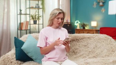 Yenilgide online oyun omuzlarını kaybettikten sonra evde oturup akıllı telefon kullanan hamile bir orta yaşlı kadın. Kanepedeki beyaz kız üzgün yüzünü gösteriyor. Titreyen kafa cep telefonu ekranına bakıyor ve üzgün hissediyor..