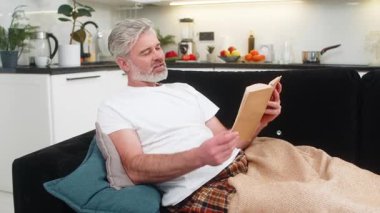 Evinde orta yaşlı bir adam ekoseli gülücüklere sarılmış kitap okur ve huzurlu boş zamanlardan ve yavaş tempodan hoşlanır. Olgun yaşlı bir adam kanepenin üzerinde ısınır sayfalarca ısınır sakin nefes alır sakin gözler dinlenir.