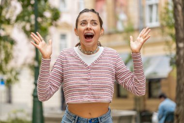 Dişlerinde diş teli olan sinirli, beyaz bir kadın stres yüzünden çığlık atıyor. Korku, çaresizlik, şaşkınlık, şaşkınlık, öfke, açık hava şoku ifade ediyor. Şehir caddesinde bir kız