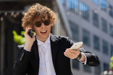 Kafası karışmış takım elbiseli bir iş adamı ofis binasının önünde iki cep telefonuyla konuşuyor. Sinirli genç ofis çalışanı iki telefon ahizesi tutuyor ve müşterilere bağırıyor..