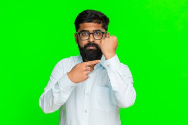 Hintli adam, güçlü bir ifadeyle yumruğunu sıkar. Açık bir kararlılıkla tehdit eder. Arap adam yeşil krom anahtar arka planda izole edilmiş. Gücü ifade ediyor, duygusal meydan okumayı zorluyor.