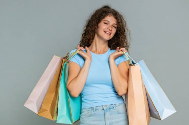 Alışverişten sonra alışveriş çantalarını mutlu bir şekilde tutan genç bir kadın. Çekici indirimler yapıyor, satış kampanyasını destekliyor. Kız neşeli bir şekilde seyirciyi alışverişe teşvik ediyor, neşeli olumlu duygular gösteriyor..