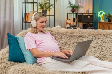 Evde orta yaşlı hamile bir kadın kulaklık takıyor. Dizüstü bilgisayarda evrak düzenliyor. Serbest çalışıyor. Kanepede oturan beyaz kız müziği sever. Görevleri bitirir. Neşeli, sakin, yumuşak akşam havası..