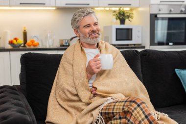 Evde orta yaşlı bir adam çay fincanının üstünde ellerini ısıtıyor hafif bir koku soluyor küçük bir yudum alıyor, hafifçe gülümsüyor. Olgun bir adam kanepeye kıvrılır omuzlarına ekose geçirir rahatlar yavaş nefes alır huzur içinde dinlenir