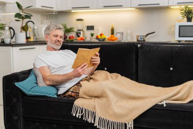 Evinde orta yaşlı bir adam ekoseli gülücüklere sarılmış kitap okur ve huzurlu boş zamanlardan ve yavaş tempodan hoşlanır. Olgun yaşlı bir adam kanepenin üzerinde ısınır sayfalarca ısınır sakin nefes alır sakin gözler dinlenir.