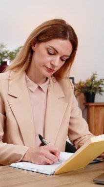 Merkez ofisteki orta yaşlı iş kadını liderlik kitabından alıntılar okuyor, gülümsüyor ve defterine fikirler yazıyor. Masadaki serbest çalışan kız hedefleri iş ve kişisel gelişim motivasyonu ve odaklanması için ipuçlarına dikkat çekiyor