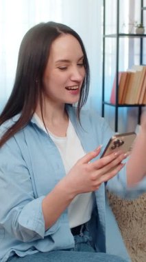 Genç ve mutlu bir kadın akıllı telefonuyla kanepede oturuyor piyangoyu sevinçle kutluyor ekranda heyecanlı görünüyor. Kafkasyalı kız neşeli duygular ifade ediyor, başarılı sonuçlardan sonra mutluluk.