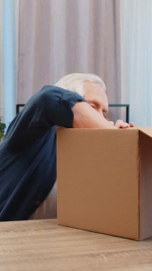 Evde kulaklıklarla teslimat paketini açan mutlu kıdemli adam. Gülümseyen büyükbaba alışverişçisi, çevrimiçi dükkan müşterisi karton kutu açıyor hızlı posta yoluyla satın alma hediyesi alıyor