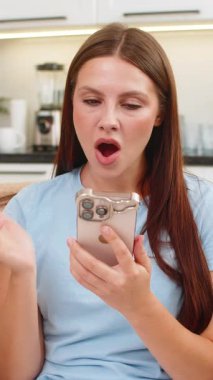 Evdeki genç kadın akıllı telefonda dil uygulaması kullanıyor kısa cümleleri tekrarlıyor ve odaklı kelimeler kuruyor. Kanepede oturan beyaz bir kız skor serisi alıyor ve rozet gelişimi kutluyor ve sevinçle gülümsüyor.