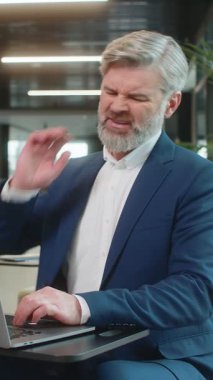 Kafkasyalı orta yaşlı işadamı ofis lobisinde dizüstü bilgisayarla çalışırken omurga kası ağrısından muzdarip. Çok çalışıyorum. Erkek girişimci, takım elbiseli adam masaj yaparak acıyı azaltmaya çalışıyor..