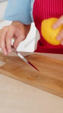 Mutfakta genç bir kadın, bir sürahi suya yakın bıçakla ahşap kesme tahtasıyla limon kesiyor. Önlükteki eller temiz yiyeceğe odaklan limon dilimlerini suya hazırla sağlıklı alışkanlıklar iç sakin ruh hali rutini