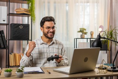 Güzel görünümlü, heyecanlı Hintli işadamı bilgisayar oyununda zaferi kutluyor yumruklarını sıkıyor, boş zamanlarını ofis masasında geçiriyor. Mutlu serbest çalışan video oyunları düzenleyici oynuyor.