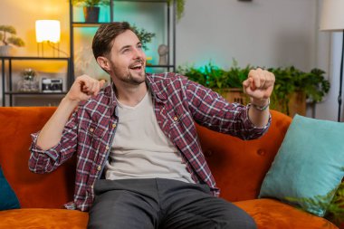 Oturma odasında kanepede otururken elleri ile şarkı söyleyip dans eden enerjik genç adam. Tasasız Kafkasyalı adam zaferi kutluyor favori müziğin tadını çıkarıyor evde tek başına eğlenirken.