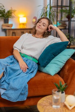 Dertsiz, genç, beyaz bir kadın evinde, kafasının arkasında kanepede rahatça oturuyor. Gülümseyen kadın, kanepede dinlenirken daire odasına bakmayı düşünüyor. Dikey