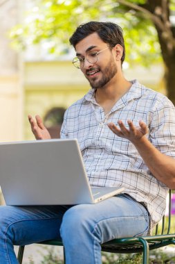 Hintli adam sandalyede oturuyor, laptop kamerasına bakıyor, arkadaşlarıyla, ailesiyle ya da müşterisiyle görüntülü bir konferans görüşmesi yapıyor, uzak sohbetin tadını çıkarıyor. İspanyol adam netbook kullanıyor. Dikey